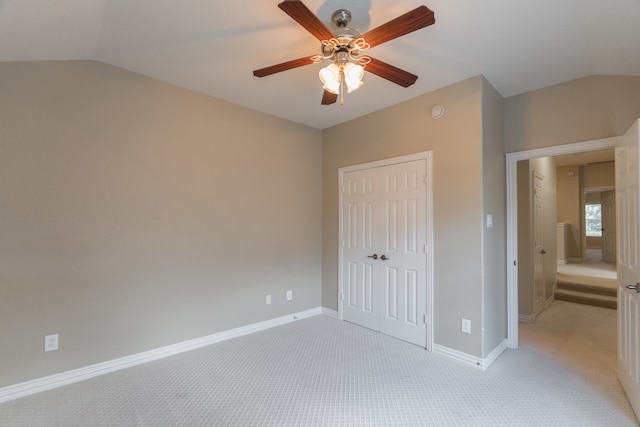 unfurnished bedroom with light carpet, a closet, lofted ceiling, and ceiling fan