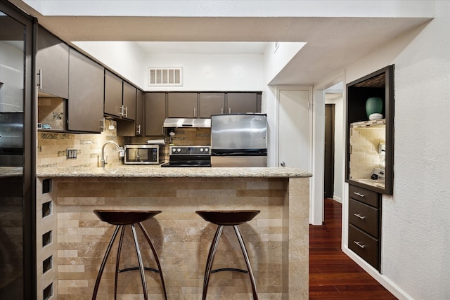 kitchen with appliances with stainless steel finishes, sink, kitchen peninsula, a kitchen breakfast bar, and dark wood-type flooring