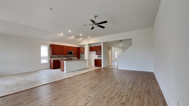 kitchen with light hardwood / wood-style floors, tasteful backsplash, lofted ceiling, stainless steel appliances, and a center island with sink