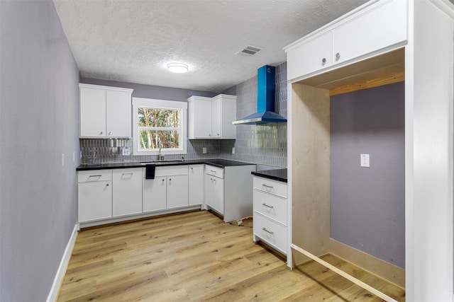 kitchen with sink, white cabinetry, wall chimney exhaust hood, tasteful backsplash, and light hardwood / wood-style flooring