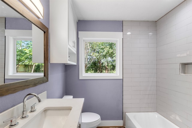 full bathroom with toilet, tiled shower / bath combo, a wealth of natural light, and vanity