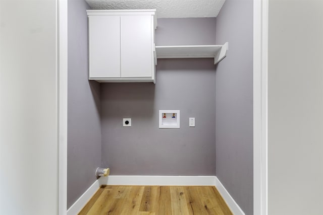 clothes washing area featuring electric dryer hookup, washer hookup, a textured ceiling, cabinets, and light hardwood / wood-style flooring