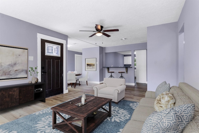 living room featuring light hardwood / wood-style floors, ceiling fan, and a textured ceiling