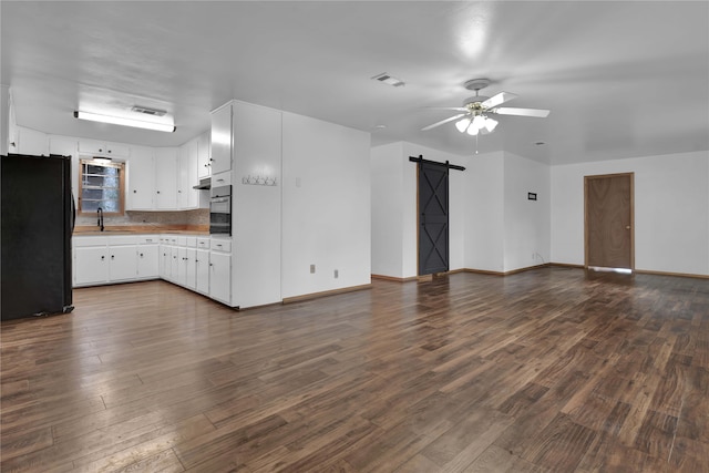 kitchen with white cabinetry, black refrigerator, dark wood-type flooring, and a barn door