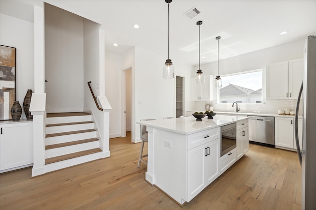 kitchen featuring pendant lighting, a kitchen island, light hardwood / wood-style flooring, white cabinetry, and appliances with stainless steel finishes