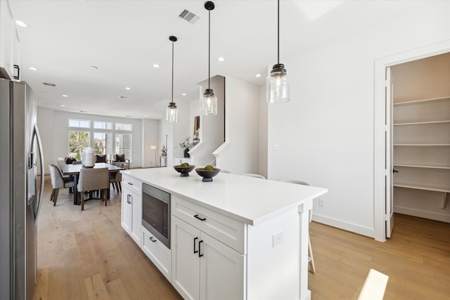 kitchen featuring white cabinetry, a kitchen island, pendant lighting, stainless steel appliances, and light hardwood / wood-style flooring