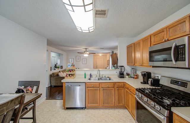 kitchen with kitchen peninsula, stainless steel appliances, a textured ceiling, ceiling fan, and sink