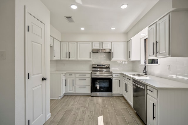 kitchen featuring light wood-type flooring, sink, white cabinetry, decorative backsplash, and appliances with stainless steel finishes