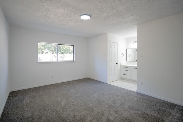 unfurnished bedroom with a closet, light colored carpet, ensuite bathroom, and a textured ceiling