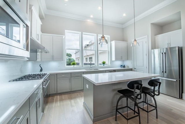 kitchen with appliances with stainless steel finishes, a kitchen bar, a center island, light hardwood / wood-style flooring, and decorative light fixtures