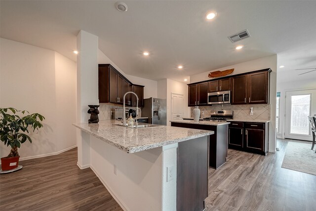 kitchen with light stone counters, kitchen peninsula, backsplash, appliances with stainless steel finishes, and light wood-type flooring