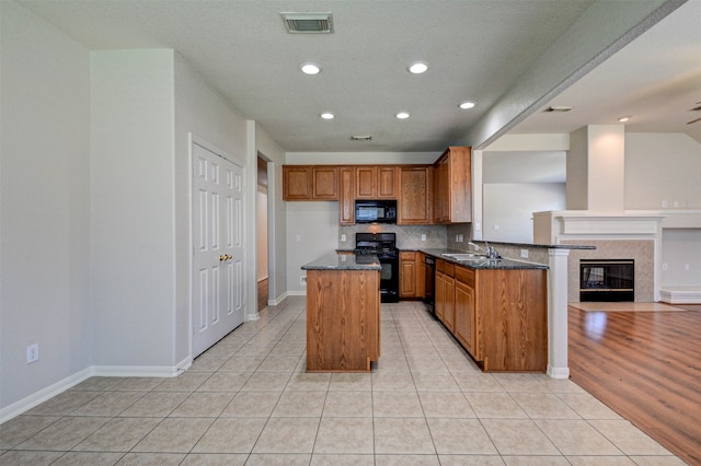 kitchen with light tile patterned flooring, a tile fireplace, kitchen peninsula, black appliances, and sink