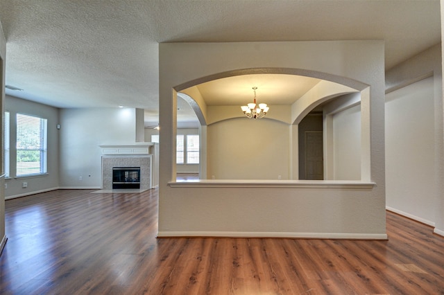 unfurnished living room with a textured ceiling, dark hardwood / wood-style floors, a chandelier, and a tile fireplace