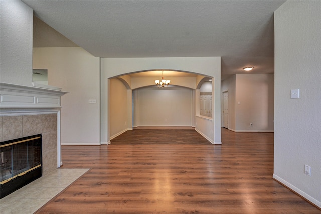 unfurnished living room featuring an inviting chandelier, dark hardwood / wood-style floors, a textured ceiling, and a tile fireplace