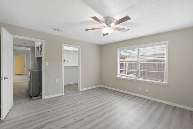 unfurnished bedroom with light wood-type flooring, a closet, a textured ceiling, a walk in closet, and ceiling fan