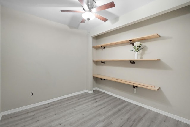 empty room with built in desk, light hardwood / wood-style floors, and ceiling fan