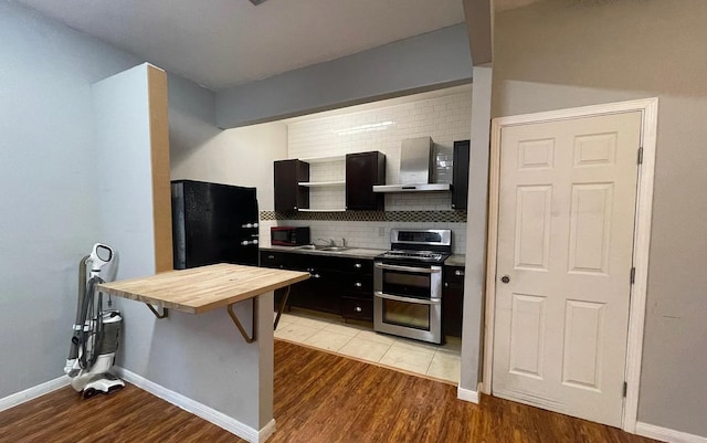 kitchen with a breakfast bar area, wall chimney exhaust hood, decorative backsplash, black appliances, and light hardwood / wood-style flooring