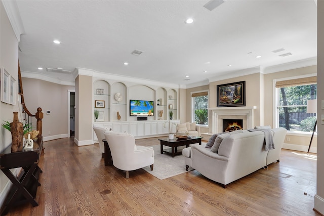 living room with built in features, ornamental molding, and light wood-type flooring