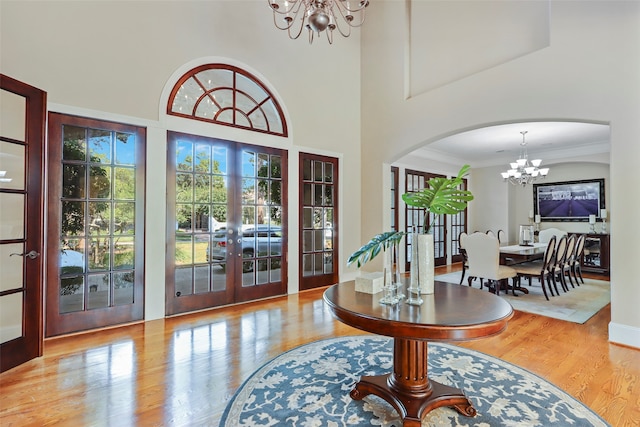 foyer entrance with light hardwood / wood-style floors, french doors, a notable chandelier, and a high ceiling