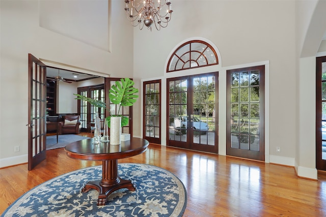 foyer entrance with hardwood / wood-style floors, french doors, ceiling fan with notable chandelier, and a high ceiling