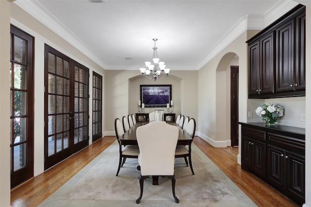 dining space featuring a chandelier, crown molding, light wood-type flooring, and french doors