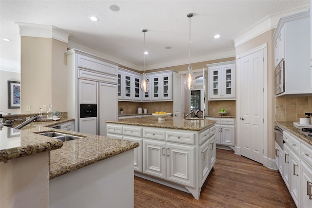 kitchen with sink, an island with sink, dark hardwood / wood-style flooring, pendant lighting, and built in appliances