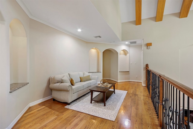 living room featuring light hardwood / wood-style floors, ornamental molding, and beamed ceiling