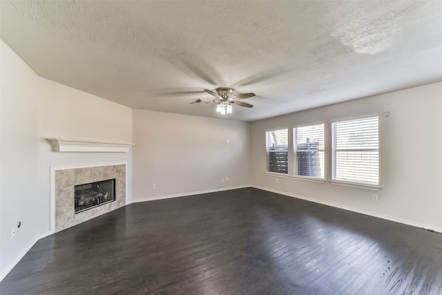 unfurnished living room with ceiling fan, a textured ceiling, a tiled fireplace, and dark hardwood / wood-style flooring