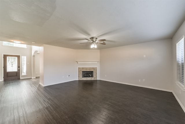 unfurnished living room with a fireplace, dark hardwood / wood-style floors, ceiling fan, and a wealth of natural light