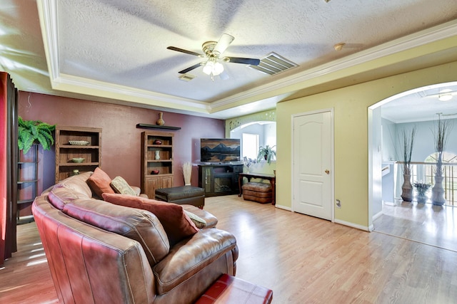 living room featuring a raised ceiling, a textured ceiling, ceiling fan, ornamental molding, and hardwood / wood-style floors