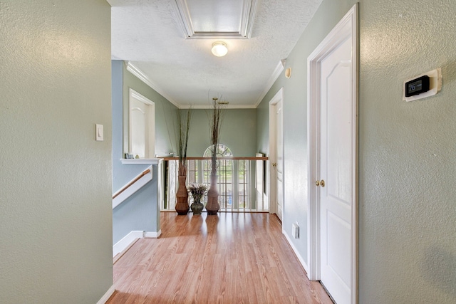 corridor with ornamental molding, light wood-type flooring, and a textured ceiling