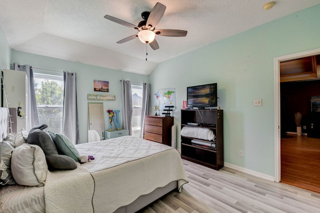 bedroom with ceiling fan, a textured ceiling, light hardwood / wood-style flooring, and lofted ceiling