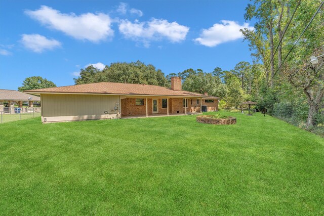 back of property with a fire pit, a yard, and a patio area