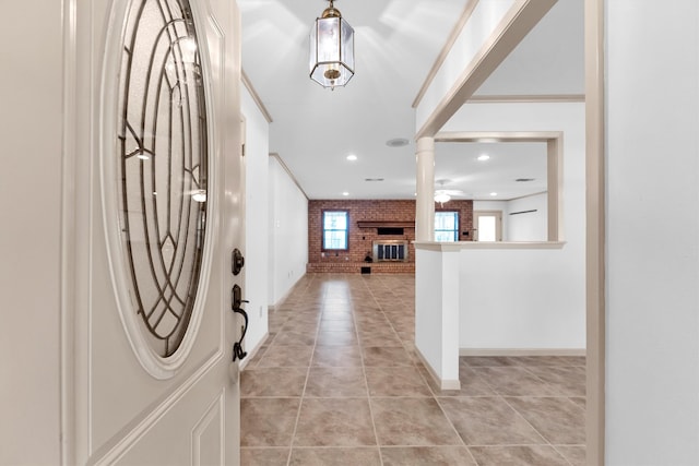 foyer entrance with ceiling fan, light tile patterned floors, ornamental molding, brick wall, and a brick fireplace