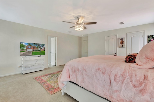 bedroom with ceiling fan, light colored carpet, and two closets