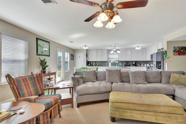 carpeted living room with ceiling fan with notable chandelier