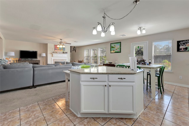 kitchen featuring pendant lighting, a center island, ceiling fan with notable chandelier, light tile patterned floors, and white cabinetry