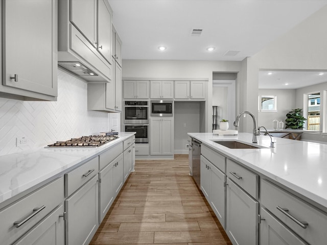 kitchen featuring light hardwood / wood-style floors, stainless steel appliances, decorative backsplash, light stone counters, and sink