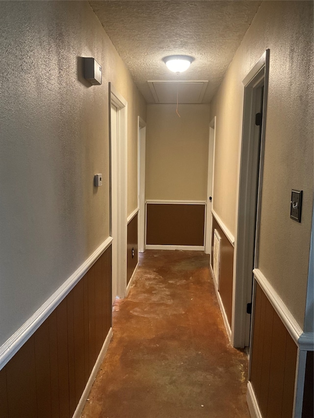 corridor with wooden walls, a textured ceiling, and concrete floors