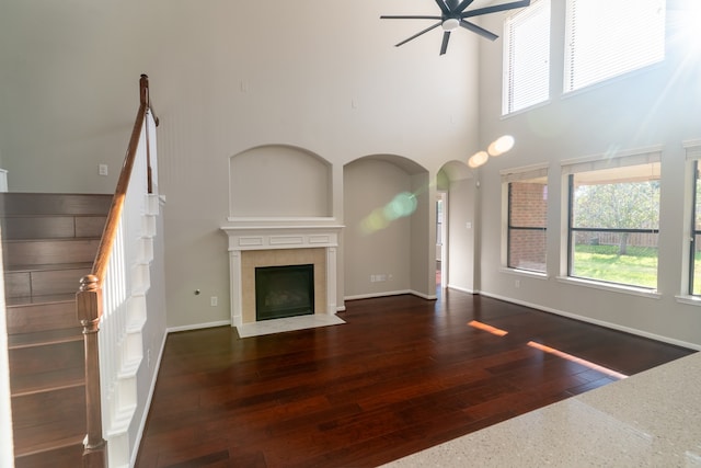 unfurnished living room featuring a high ceiling, a tiled fireplace, ceiling fan, and dark wood-type flooring