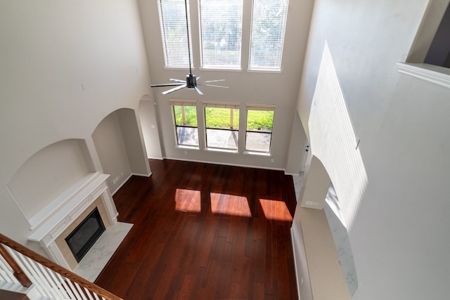 unfurnished living room featuring a premium fireplace, a towering ceiling, ceiling fan, and dark wood-type flooring