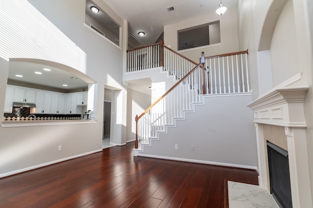 unfurnished living room featuring a towering ceiling, a high end fireplace, and dark hardwood / wood-style flooring