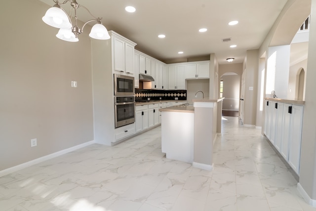 kitchen with decorative light fixtures, a center island with sink, stainless steel appliances, and white cabinets