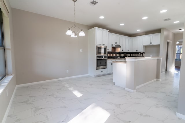 kitchen with white cabinets, backsplash, decorative light fixtures, a center island with sink, and a notable chandelier