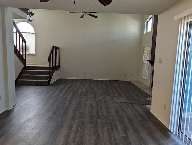 unfurnished living room with ceiling fan, a textured ceiling, dark wood-type flooring, and a large fireplace