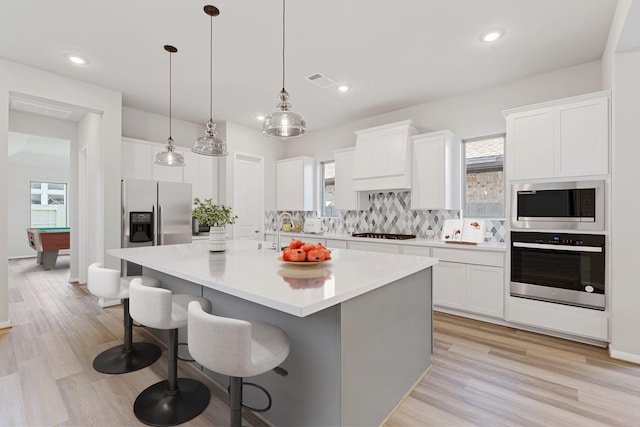 kitchen featuring stainless steel appliances, a spacious island, light countertops, decorative backsplash, and white cabinets