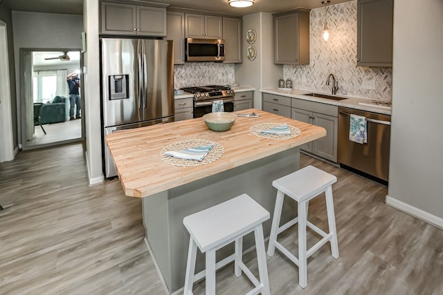 kitchen featuring appliances with stainless steel finishes, gray cabinetry, light hardwood / wood-style floors, a breakfast bar, and sink