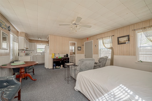 bedroom with carpet, white refrigerator, wood walls, and ceiling fan