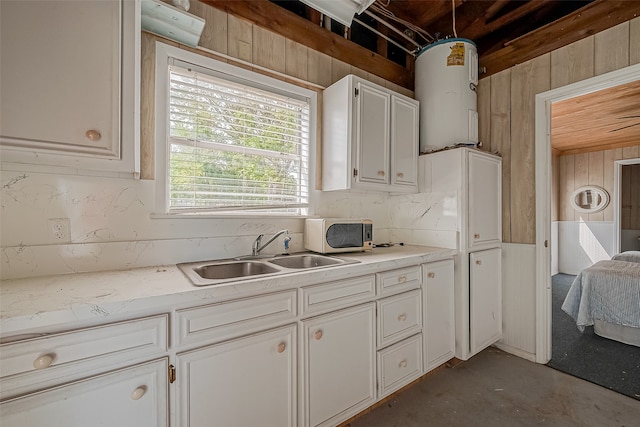 kitchen featuring water heater, wooden walls, sink, and white cabinetry