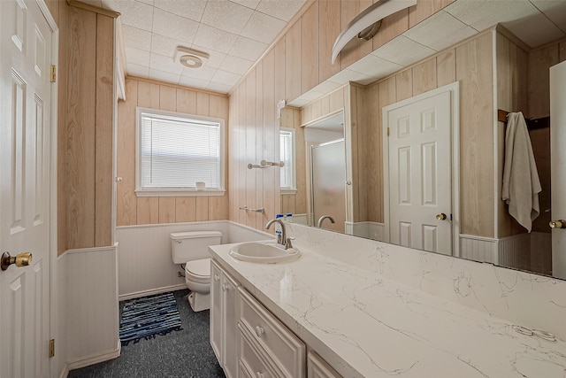 bathroom featuring wooden walls, vanity, toilet, and a shower with door